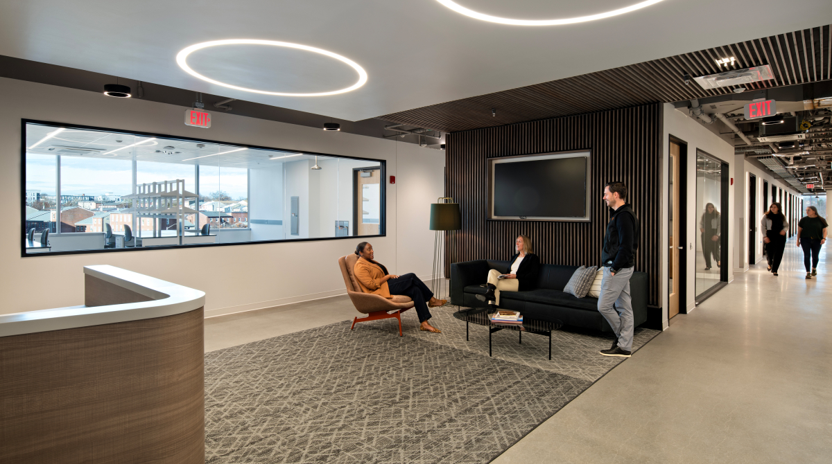 Three people talking in the lobby of an office suite with a wet laboratory in the background
