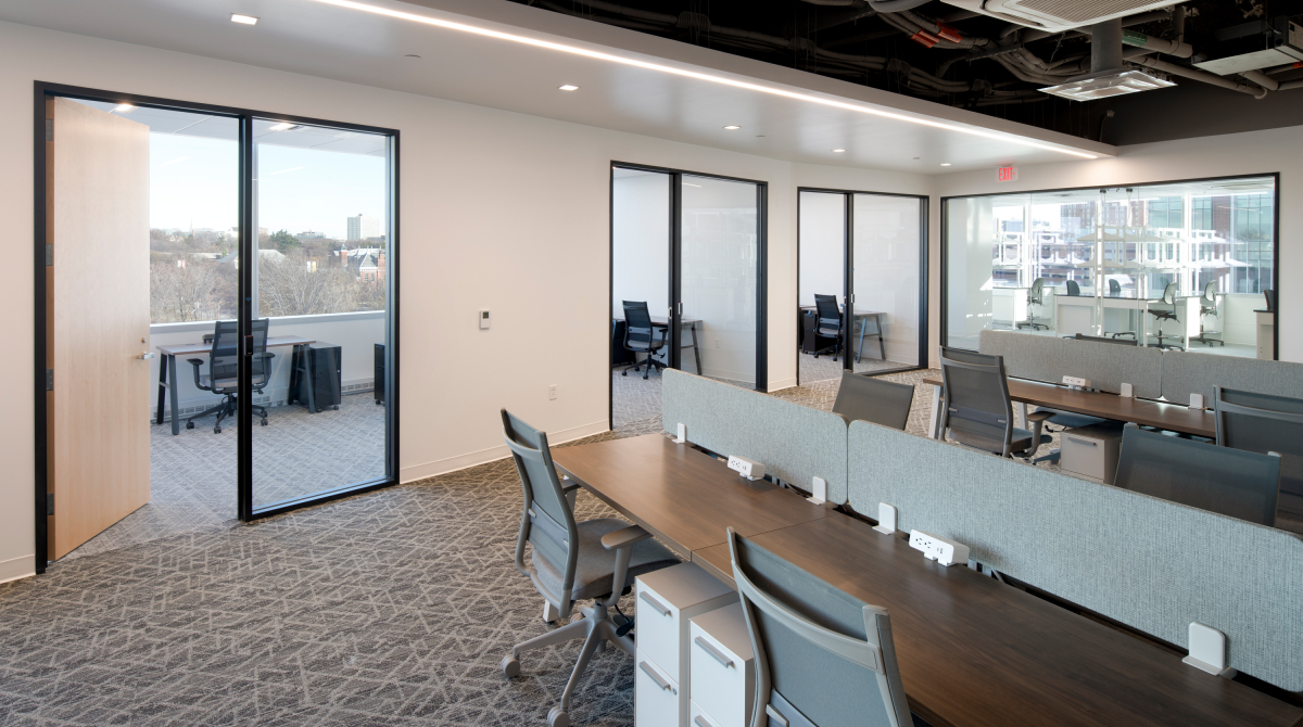 Empty open concept office with desks and chairs in the foreground and offices wtih doors in the background