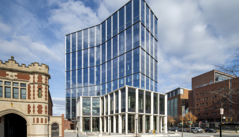 Picture of a tall, glass covered commercial building with a historic firehouse to the left and brick buildings to the right
