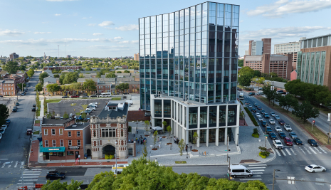 Tall glass building next to a historic firehouse and rowhome style buildings