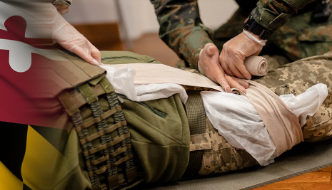 Milatary person simulating applying pressure to dress a wound to the upper leg